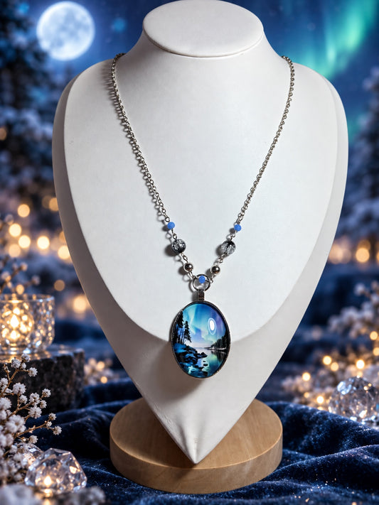 Silver-tone necklace with blue and black-and-clear beads and an oval pendant showing northern lights over a woodland lake.