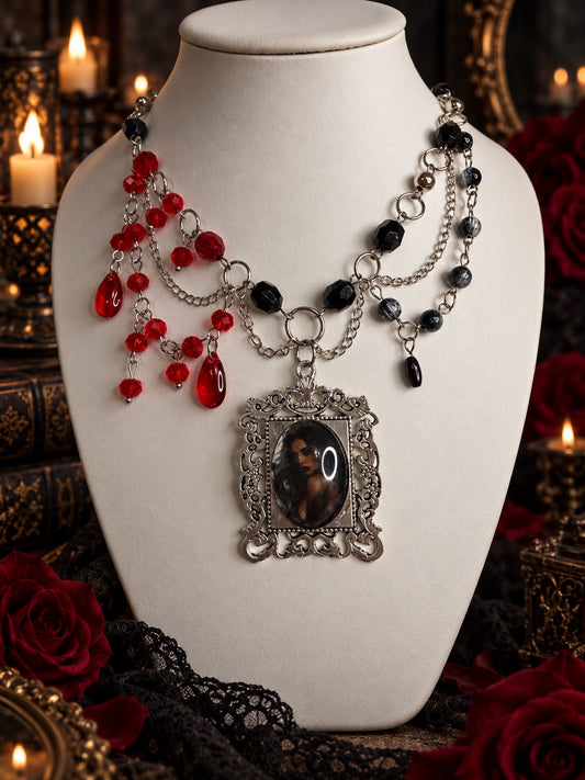 Asymmetric red and black beaded necklace with draped silver-tone chains and an ornate framed dark portrait pendant
