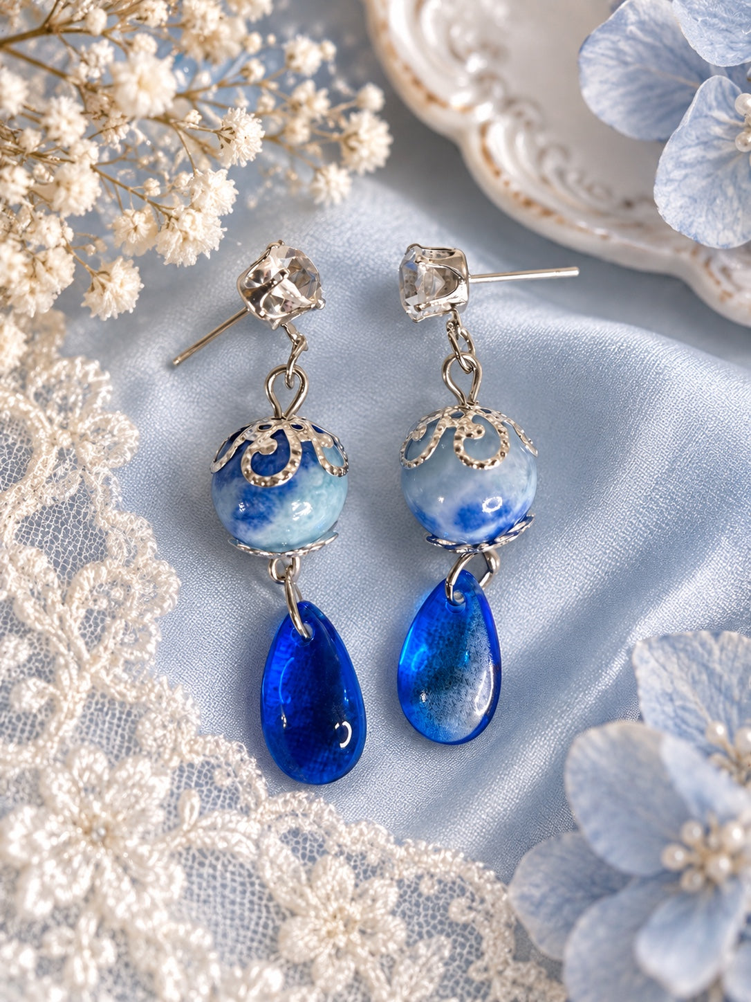 Blue drop earrings with clear faceted studs, blue-and-white marbled round beads, silver-tone bead caps and deep blue teardrops