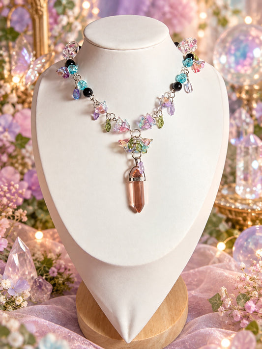 Fairycore necklace with pastel butterfly charms, green and purple leaves, aqua and black beads, and a peach-colored pointed pendant in a silver-tone setting.