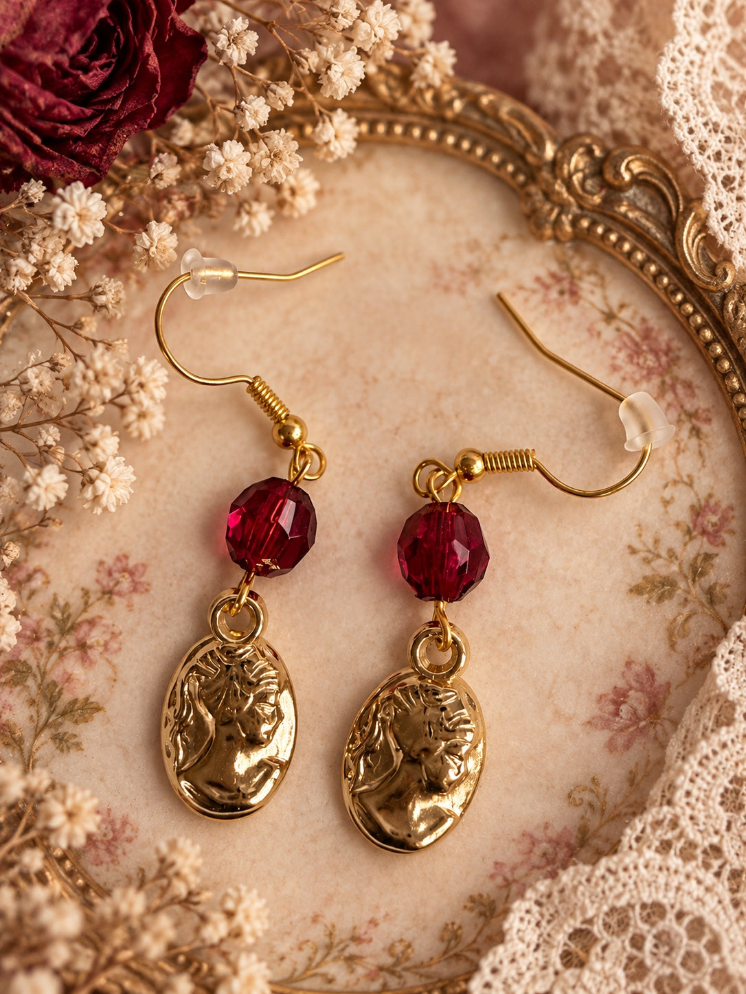 Gold-tone oval portrait earrings with deep red faceted beads and French hooks