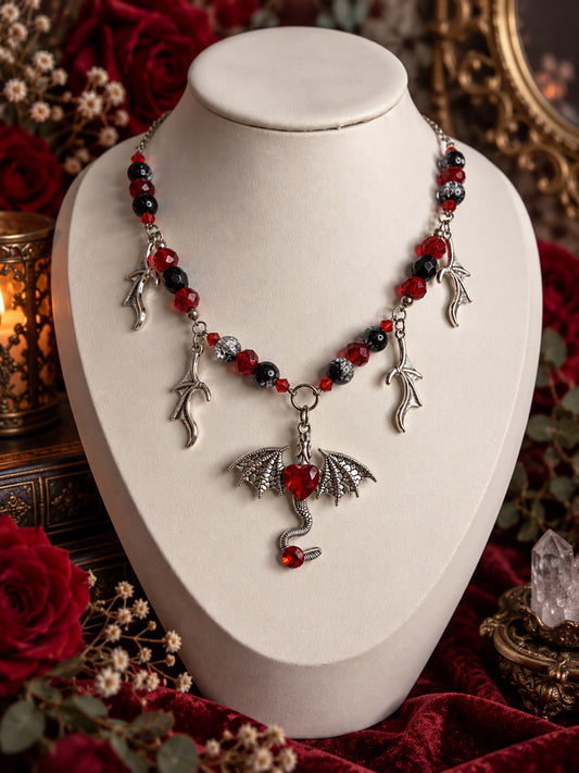 Red and black beaded necklace with silver-tone curved charms and a winged dragon pendant featuring a red heart and curled tail.