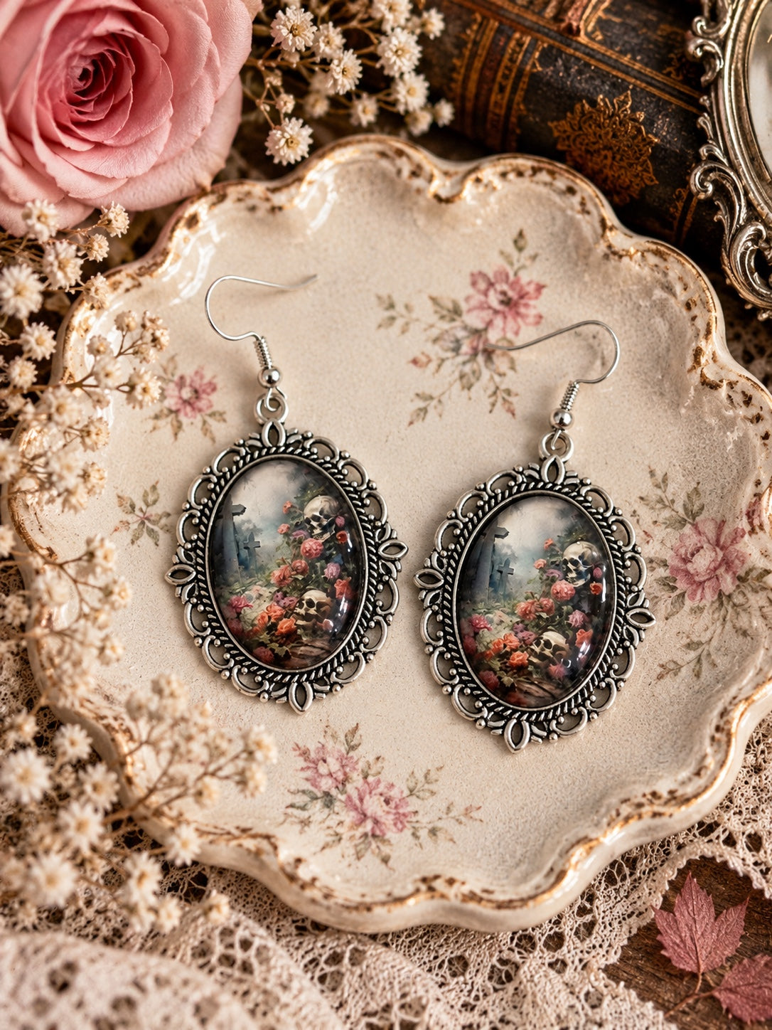 Silver-tone oval cameo earrings depicting skulls, roses and a misty graveyard, with French hooks