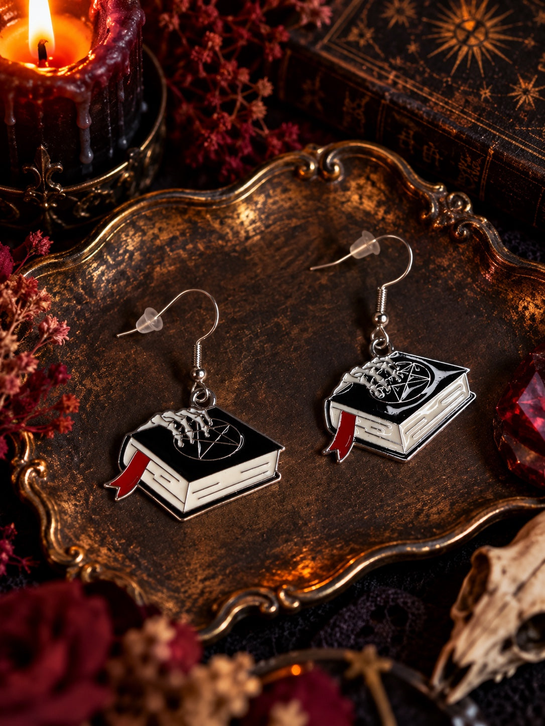 Black spellbook earrings with white pages, red bookmarks, pentagram and skeletal hand details on silver-tone French hooks