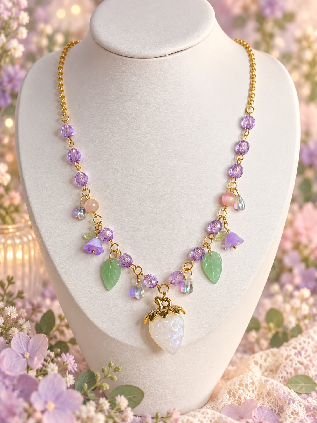 Gold-tone necklace with lilac beads, purple flowers, green leaves and a pearlescent white strawberry pendant.