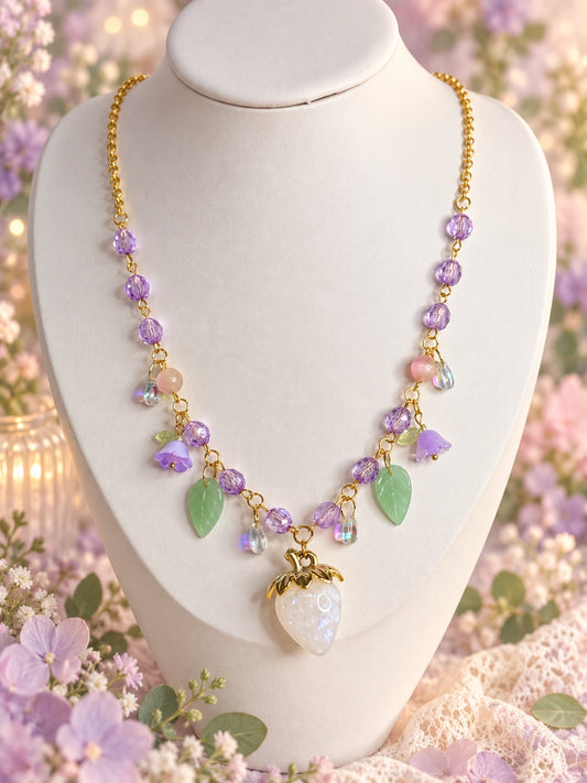 Gold-tone necklace with lilac beads, purple flowers, green leaves and a pearlescent white strawberry pendant.