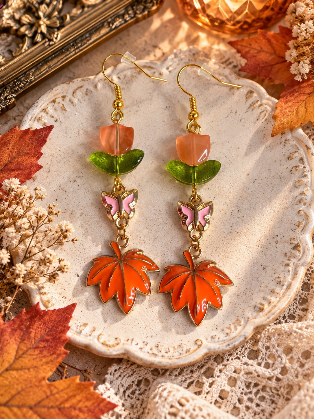 Gold-tone earrings with peach tulip beads, green leaves, pink butterflies and orange maple leaf charms
