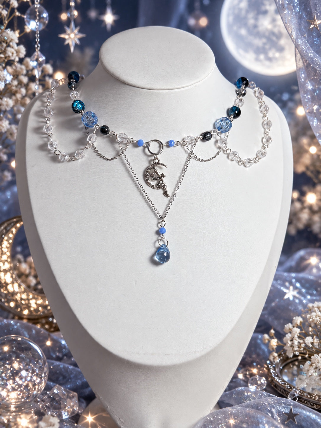 Layered silver-tone necklace with blue, dark and clear beads, draped beaded strands, a fairy on a crescent moon and a blue teardrop pendant.