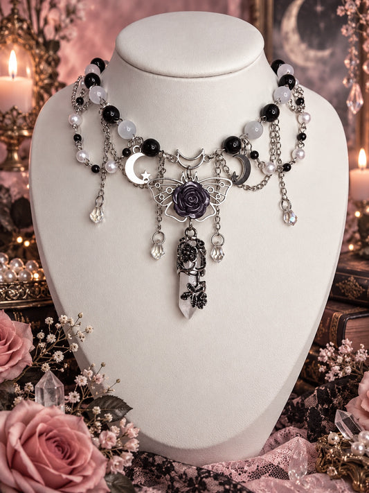 Black and white layered necklace with silver-tone crescents, an openwork moth with a dark rose, and a pale pointed pendant wrapped in dark floral metalwork.