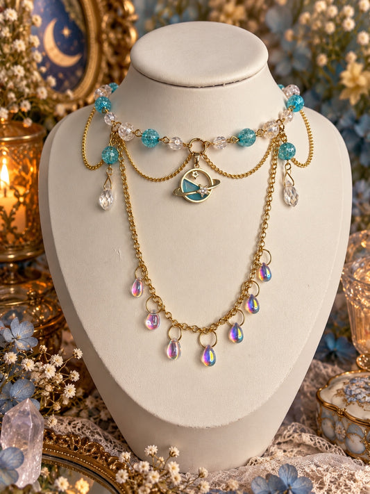 Gold-tone celestial necklace with aqua and clear beads, a ringed planet pendant, draped chains and iridescent teardrops