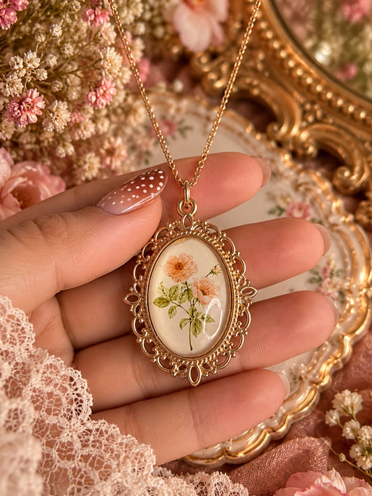 Peachblossom Heirloom Necklace with peach flowers and green leaves in an ornate warm gold-tone oval frame
