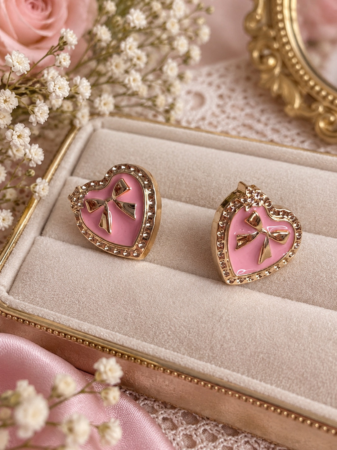 Pink heart-shaped gold-tone stud earrings with raised bow details