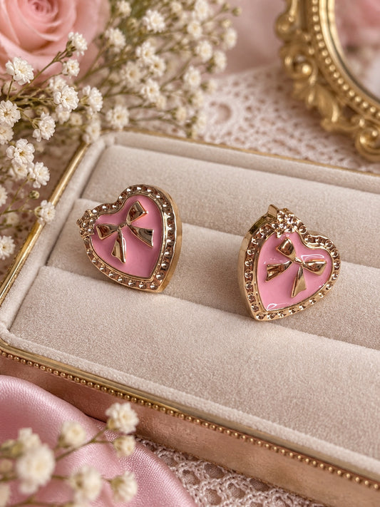 Pink heart-shaped gold-tone stud earrings with raised bow details