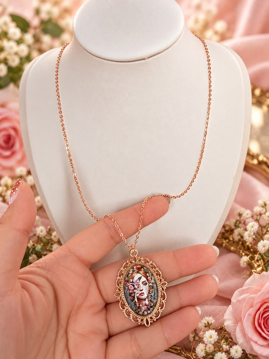 Rose-gold-tone necklace with ornate oval frame and a floral feminine portrait pendant