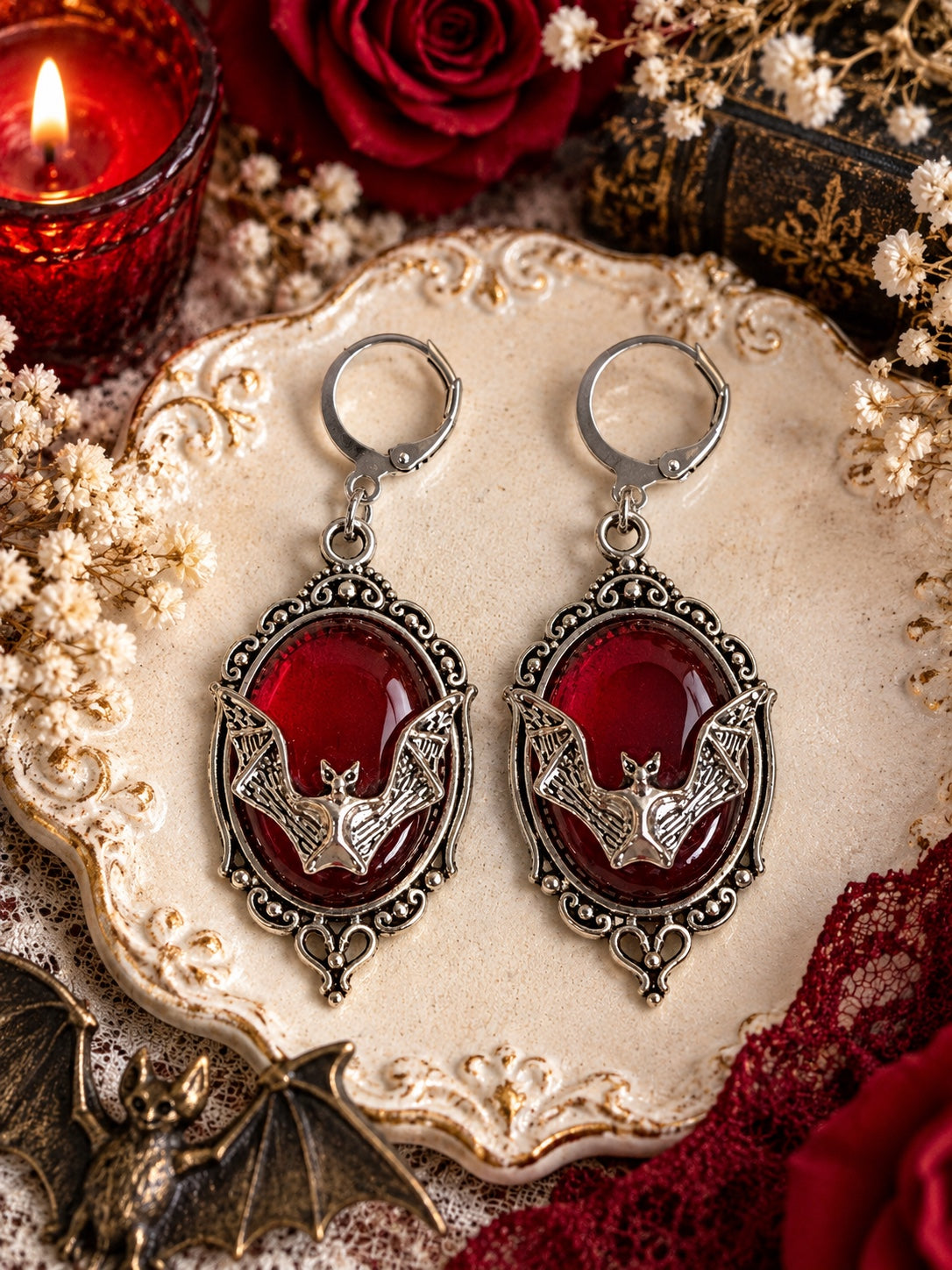 Silver-tone bat earrings with deep red oval cabochons, ornate frames and leverback closures