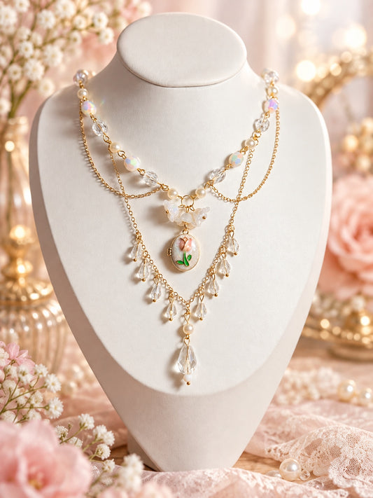 Layered gold-tone necklace with clear and iridescent beads, cream pearl-style accents, white flowers, an oval pink tulip pendant and dangling clear teardrops.