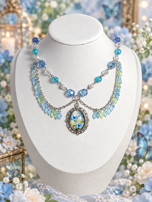 Layered silver-tone necklace with blue and aqua beads, faux pearls, blue and green leaf charms and an ornate blue butterfly illustration pendant.