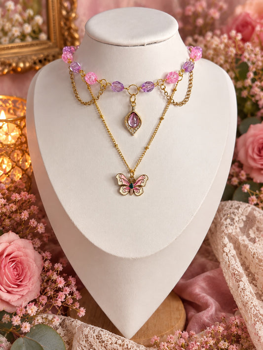 Layered gold-tone necklace with pink and lilac beads, a purple teardrop and a pink butterfly pendant.