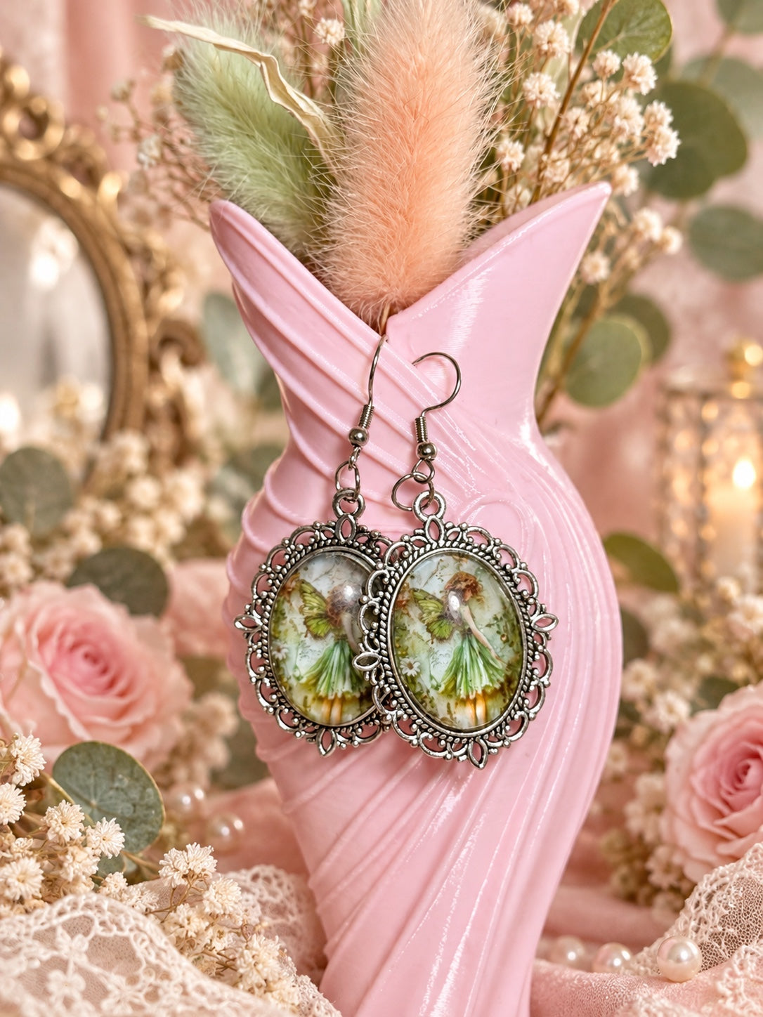 Silver-tone ornate oval fairy cameo drop earrings with a green fairy illustration and fishhook ear wires.