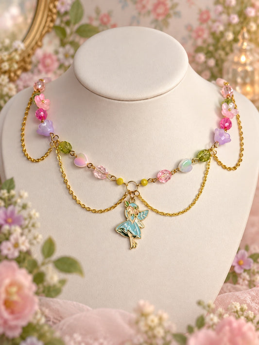 Gold-tone necklace with a blue fairy pendant, pastel flower and heart beads, pink and green beads and draped chains.