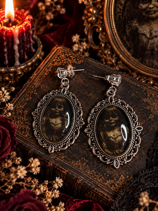 Ornate silver-tone oval earrings with haunting doll portraits and clear decorative stud tops.