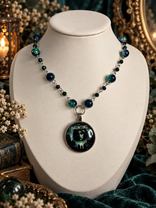 Horror necklace with blue-green round beads, dark faceted beads and a round silver-tone pendant featuring The Haunting artwork.