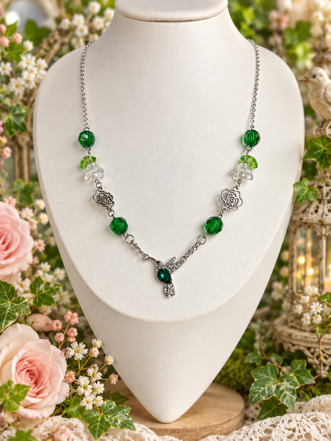 Silver-tone necklace with deep green beads, clear flower details, openwork roses and a sparkling hummingbird with a green centre.