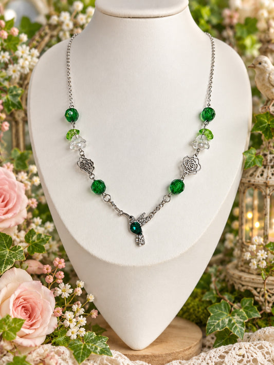 Silver-tone necklace with deep green beads, clear flower details, openwork roses and a sparkling hummingbird with a green centre.