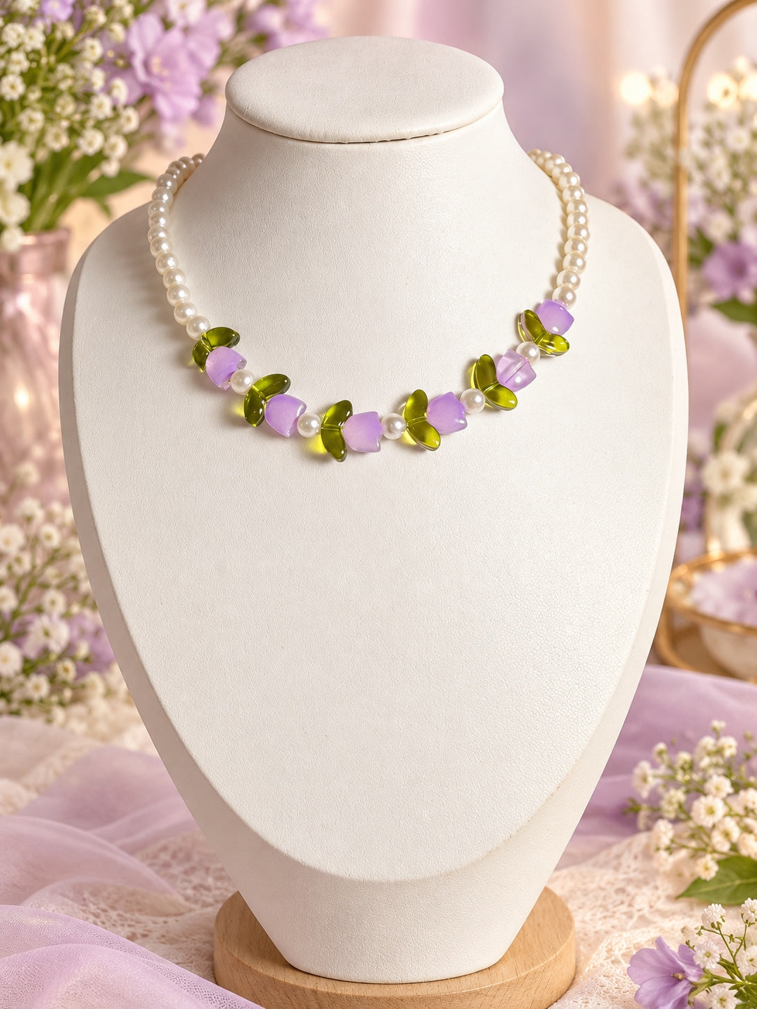 Cream pearl-style beaded necklace with lilac flower-shaped beads and translucent olive-green leaf details along the front.