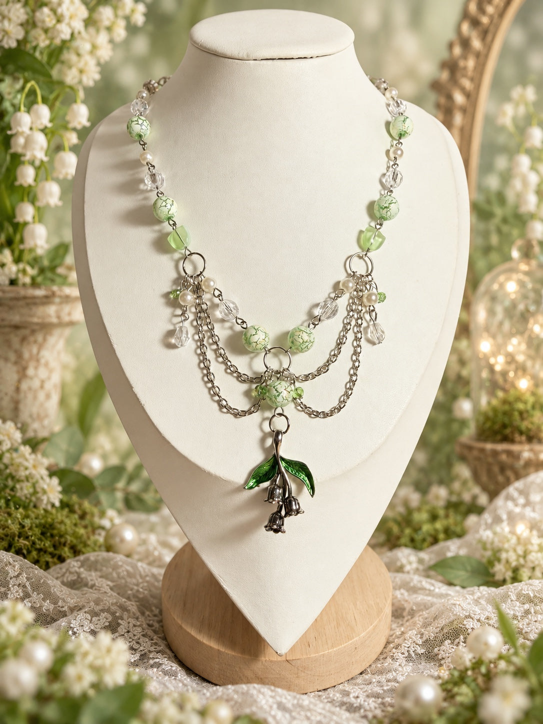 Layered silver-tone necklace with pale green patterned beads, clear faceted beads, pearl-style accents and a bell-flower pendant with green leaves.