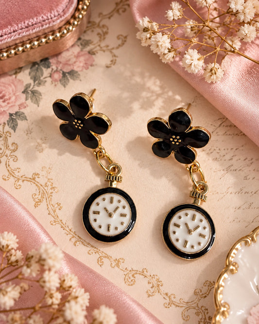 Black flower stud earrings with gold-tone edges and dangling black-and-white decorative pocket-watch charms.