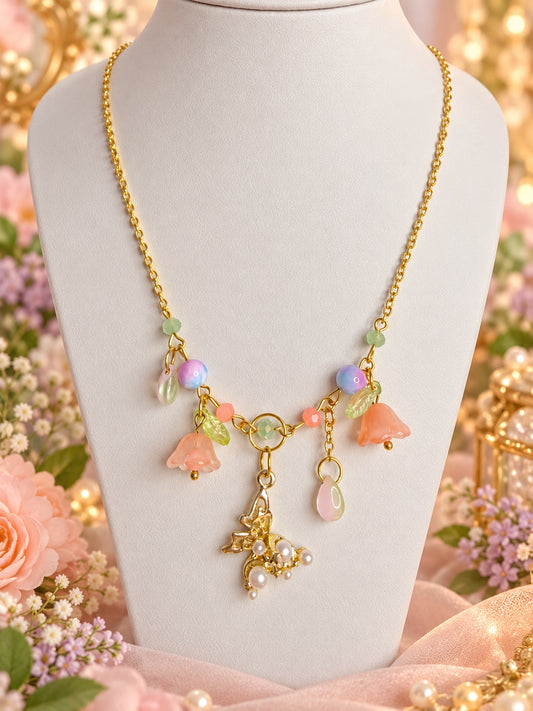 Gold-tone necklace with peach bell flowers, green leaves, pastel beads and a botanical pendant decorated with white pearl-style beads.