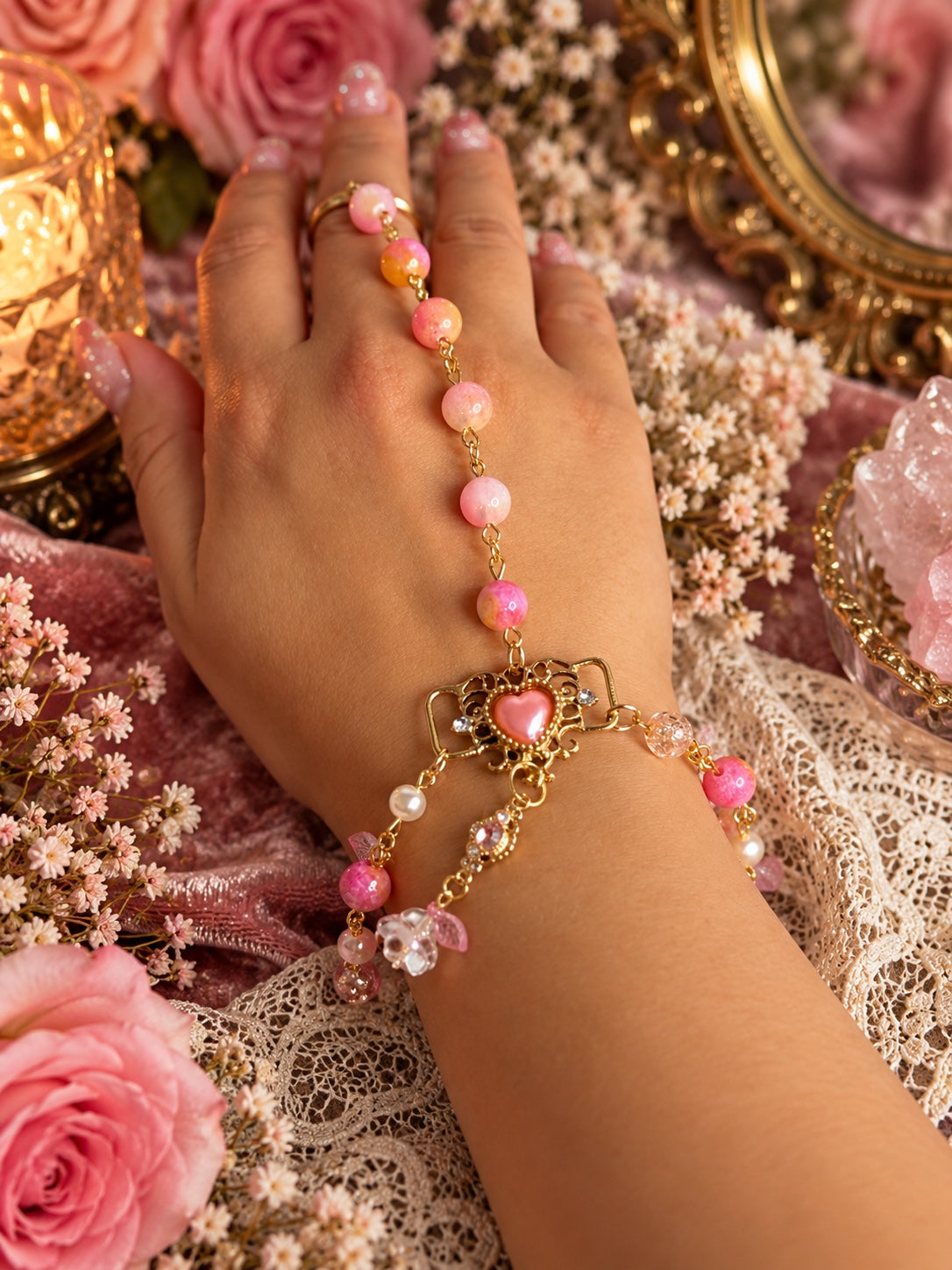 Pink and peach beaded gold-tone handchain with an ornate heart, flower and leaf charms, worn on the hand.