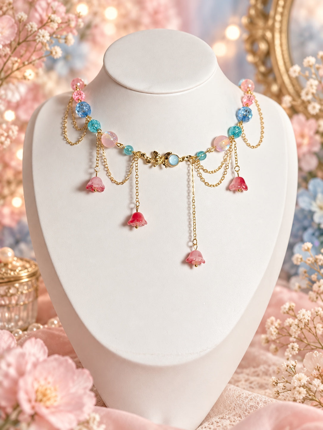 Gold-tone fairy necklace with pink, blue and aqua beads, a fairy centrepiece with a pale blue accent, draped chains and four pink bell flower drops.