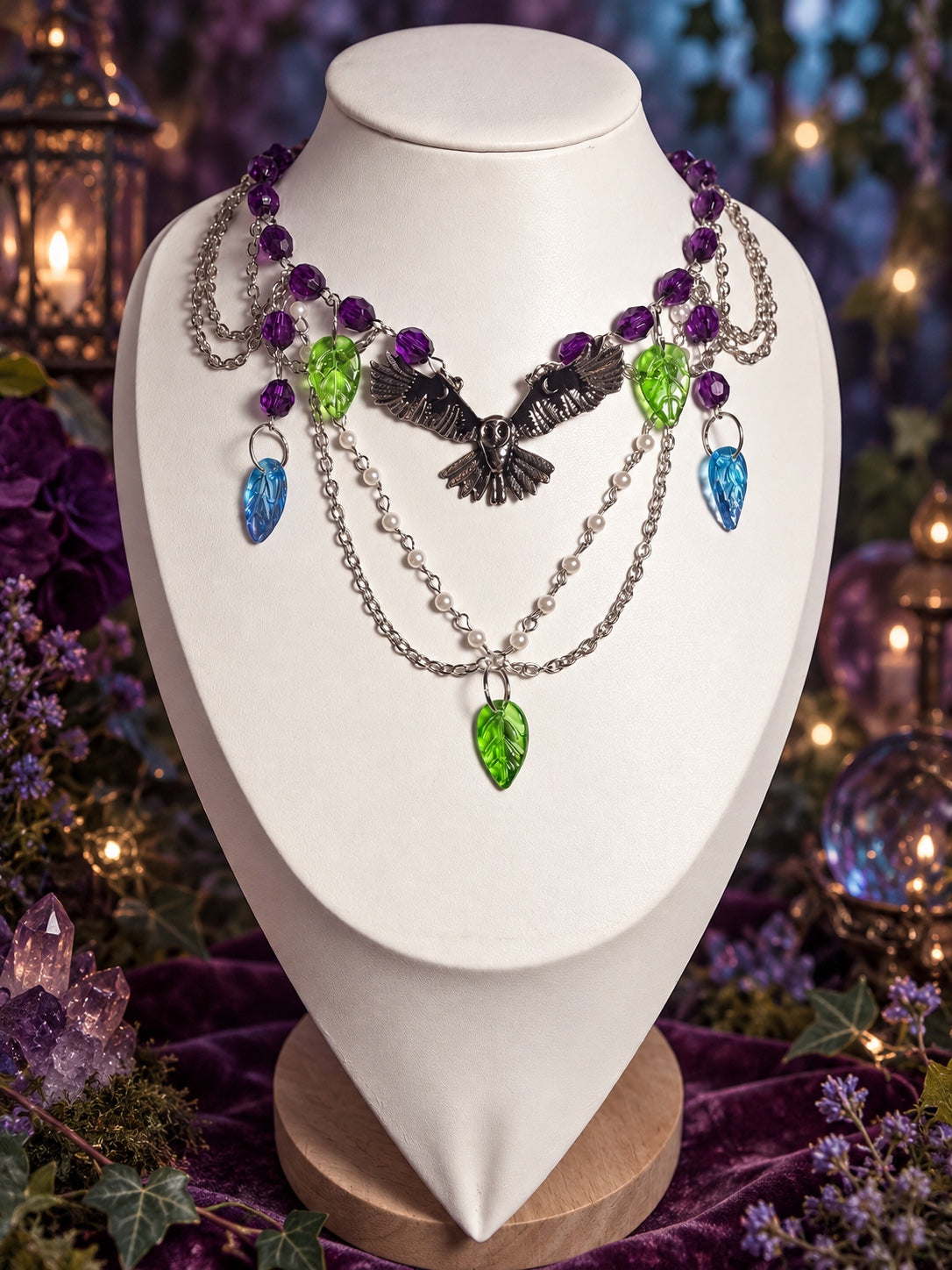Dark fairycore and witchy necklace with a dark spread-wing bird centerpiece, purple beads, white pearl-style beads, green and blue leaf charms and silver-tone chains.