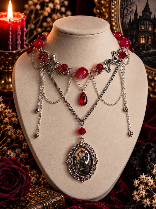 Red and silver-tone layered statement necklace with draped chains, a red teardrop and an ornate sinister clown cameo.