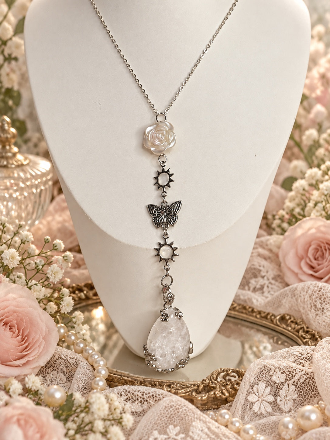 Silver-tone necklace with a pearly white rose, two sunburst links, an openwork butterfly and a large translucent white teardrop pendant.