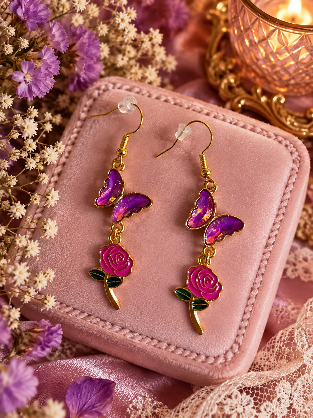 Gold-tone drop earrings with shimmering purple butterflies and pink rose charms with dark green leaves.