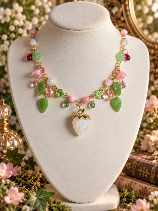Gold-tone necklace with a pearly white strawberry pendant, pink flowers, green leaves and pastel beads.