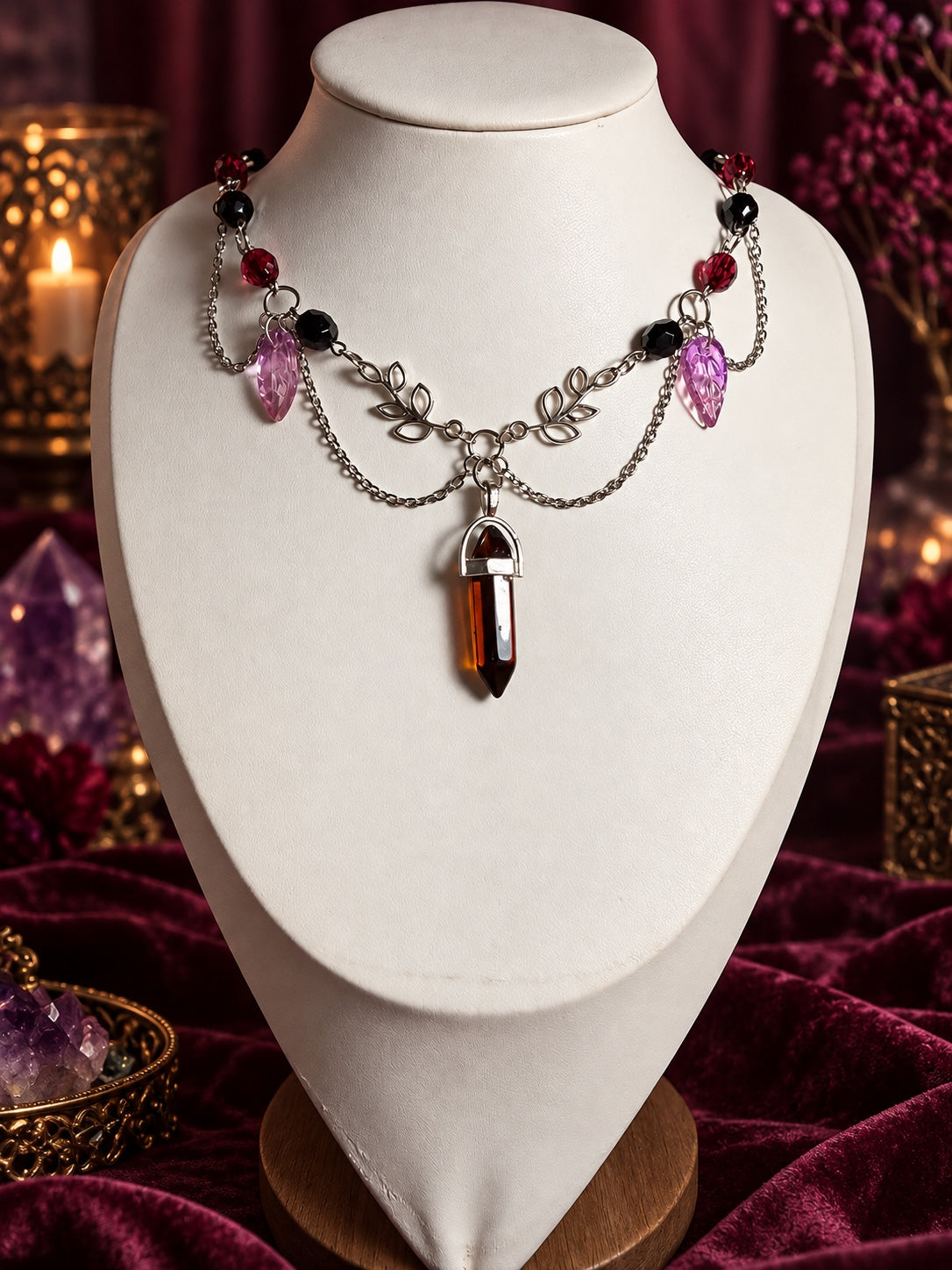 Silver-tone necklace with black and deep red beads, purple leaf charms, draped chains and a dark amber-coloured pointed pendant.