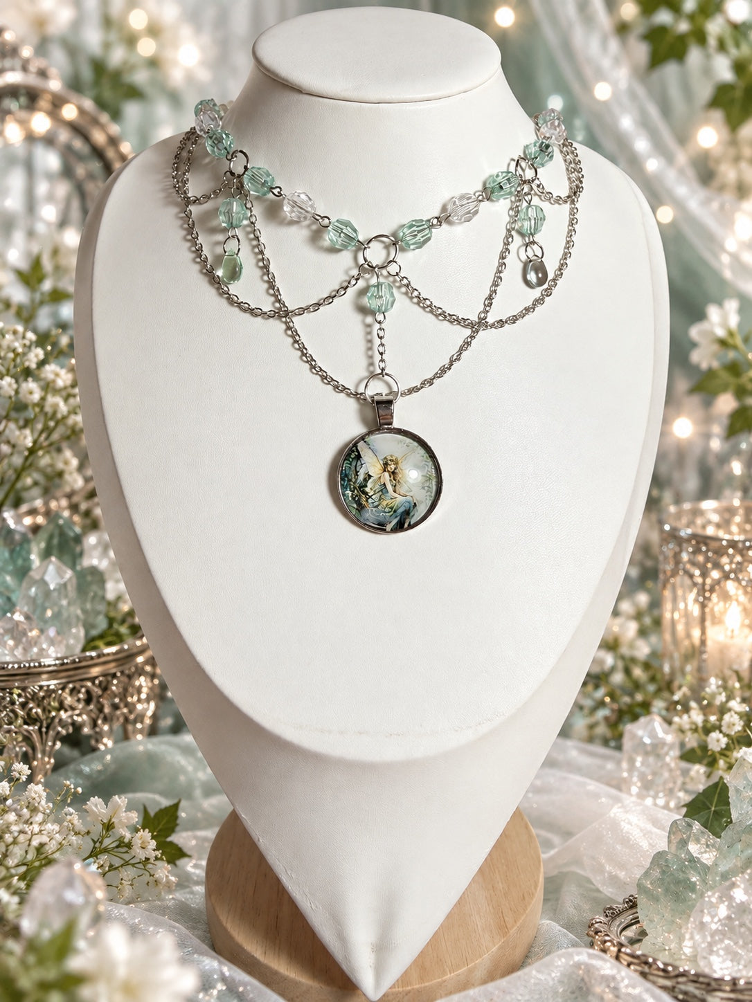Layered silver-tone necklace with pale green and clear faceted beads, small green drops, draped chains and a round illustrated fairy pendant.